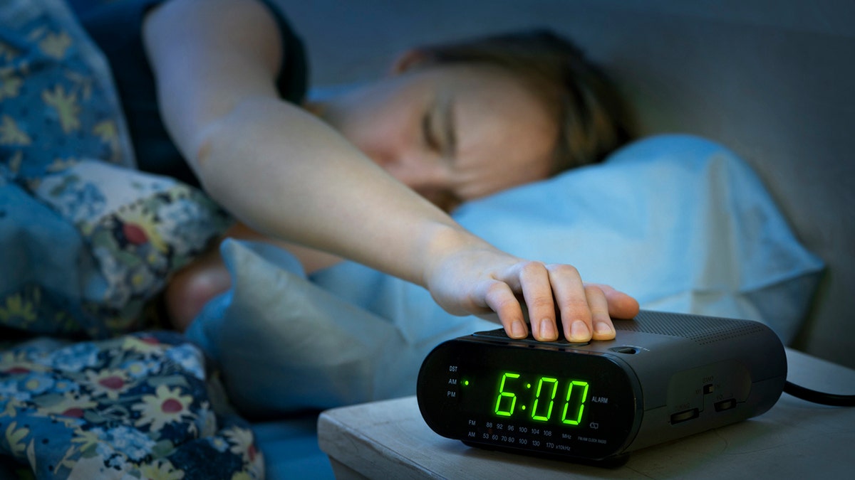 Young Woman by pressing a Snooze button in the morning digital alarm clock
