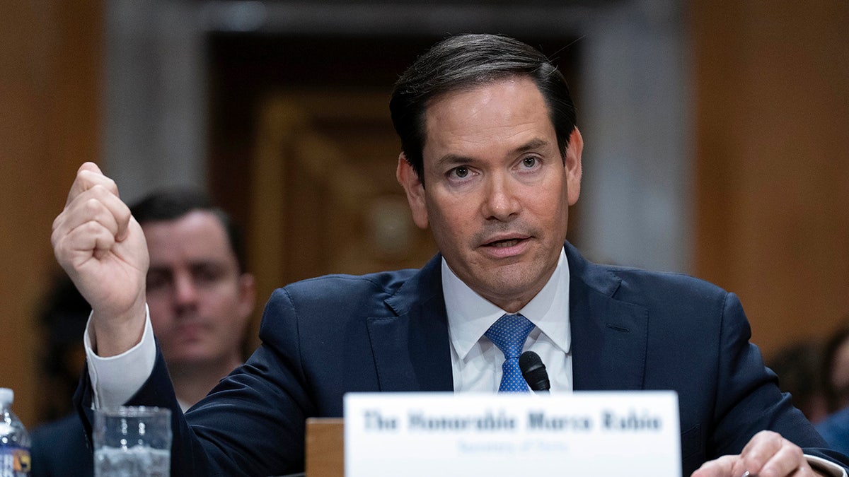 Secretary of State Marco Rubio testifying in a dark dress and a blue tie